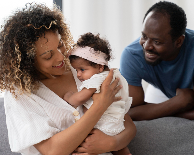 New family together in a warm, softly-lit setting, smiling with their newborn